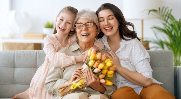 Happy mother's day. Child daughter and mother are congratulating granny giving her flowers tulips. Grandma, mum and girl smiling and hugging. Family holiday and togetherness.