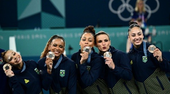 Imagem da equipe feminina do Brasil no p&oacute;dio das Olimp&iacute;adas 2024 com a medalha de bronze