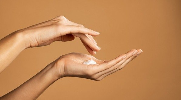 Close up shot of beautiful female hands holding and applying moisturiser. Beauty woman hand applying cream. Beautiful girl on creamy background holding moisturizer.