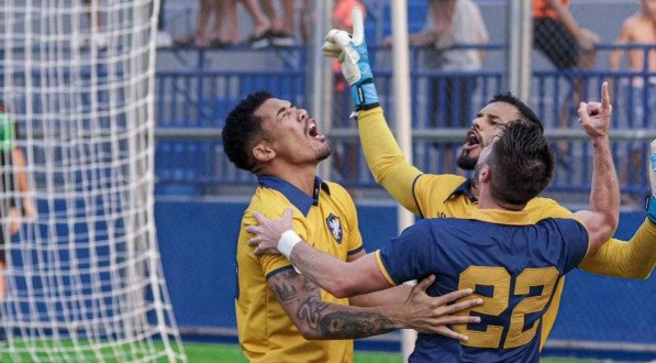 Imagem dos jogadores do Retrô de joelhos no gramado comemorando a classificação na Série D