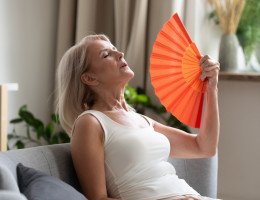 Imagem ilustrativa de mulher com o calor da menopausa, se abanando com leque laranja