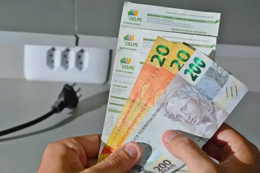 Pessoa segurando conta de luz com notas de R$ 20 e R$ 200.