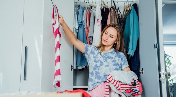 Woman selecting clothes from her wardrobe for donating to a Charity shop. Decluttering, Sorting clothes and Cleaning Up. Reuse, second-hand concept. Conscious consumer, sustainable lifestyle