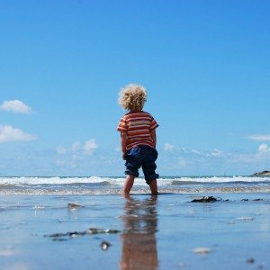 Imagem ilustrativa de uma criança brincando na praia, com o pé dentro do mar