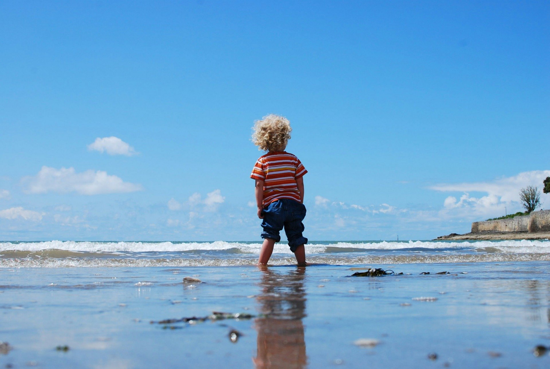 Imagem ilustrativa de uma criança brincando na praia, com o pé dentro do mar