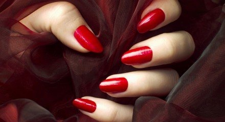 Unhas esmaltadas de vermelho segurando tecido do mesmo tom.