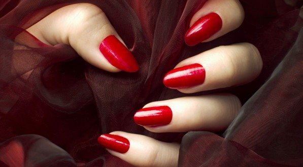 Unhas esmaltadas de vermelho segurando tecido do mesmo tom.