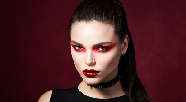 Young beautiful gothic woman with white skin and red lips with bloody drops wearing black collar with spikes. Red smokey eyes. Vampire or halloween make-up.