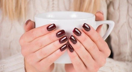 Mulher com esmalte de unhas marrom detém a xícara de café nas mãos