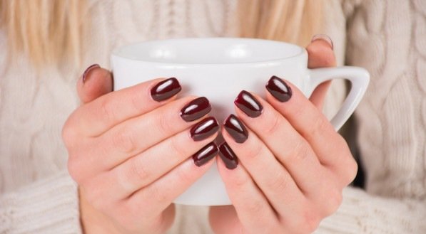 Mulher com esmalte de unhas marrom detém a xícara de café nas mãos