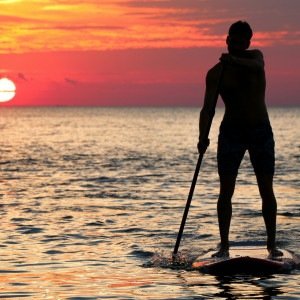 Imagem de um homem praticando stand up paddle na praia