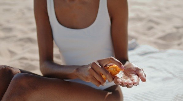 As mãos borrifam o óleo de proteção solar closeup. Menina atraente tomando sol à beira-mar