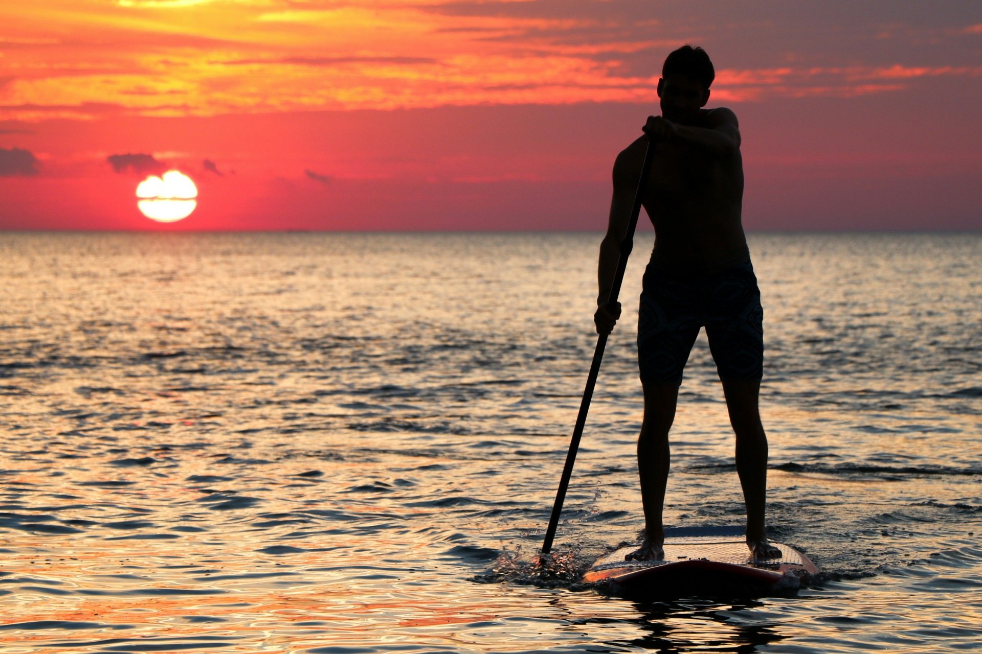 Imagem de um homem praticando stand up paddle na praia