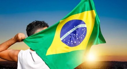 Imagem de um homem negro segurando a bandeira do Brasil no nascer do sol