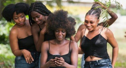 Imagem de mulheres negras olhando para um celular e sorrindo