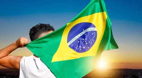 Imagem de um homem negro segurando a bandeira do Brasil no nascer do sol