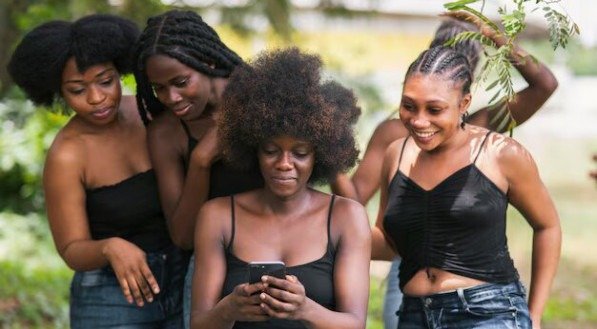 Imagem de mulheres negras olhando para um celular e sorrindo