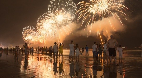 Imagem ilustra pessoas celebrando virada de ano na praia