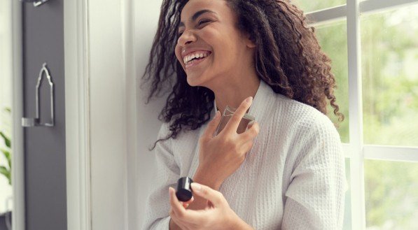 Imagem de mulher sorrindo e borrifando perfume.