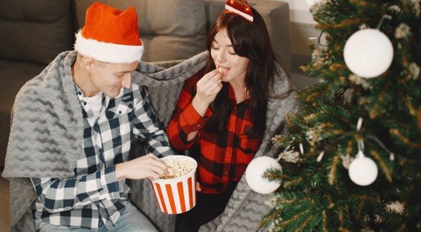 Imagem ilustrativa de um casal comendo pipoca usando roupas de natal