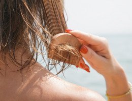 Imagem de mulher penteando seus cabelos molhados na praia.