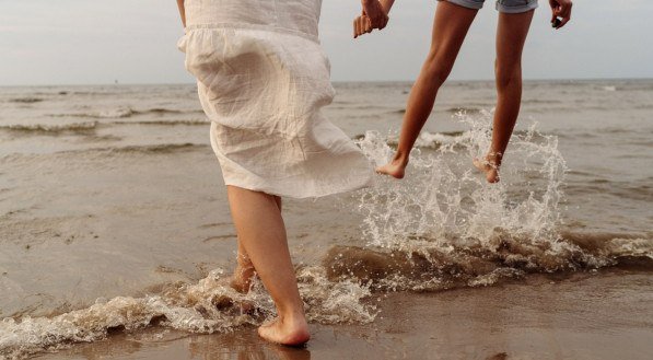 Imagem de duas mulheres pulando no mar com respingos de mãos dadas
