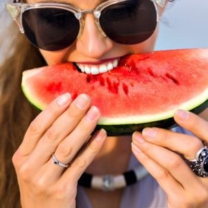 Imagem ilustrativa de uma menina comendo melancia na praia 