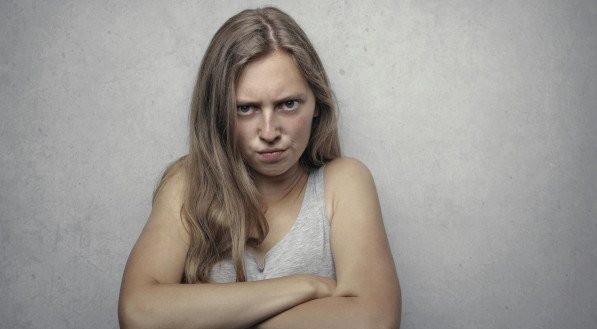 Imagem ilustrativa de uma mulher com braços cruzados, com uma expressão de irritação no rosto