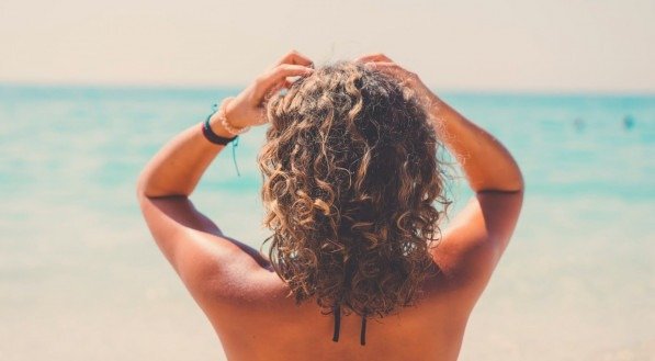 Imagem de mulher com cabelos enroladas de frente para o mar.