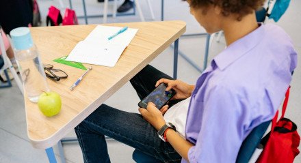 Imagem de criança usando celular em sala de aula, governo regulamenta lei que restringe uso de celular na escola