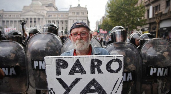 Um manifestante segura uma placa que diz em espanhol 'Greve AGORA!' na frente de policiais