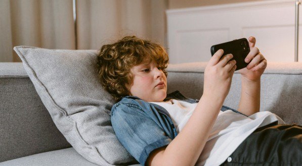 Imagem de criança usando celular. Especialista comenta nova medida do Tik Tok e os prejuízos que uso excessivo de telas podem causar a crianças e adolescentes