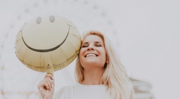 Imagem ilustrativa de uma mulher sorrindo enquanto segura um balão que também sorri