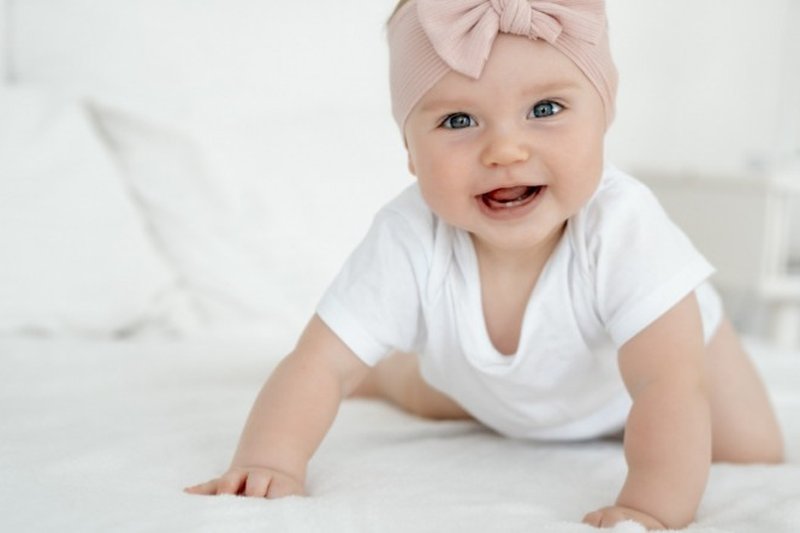 Bebê sorridente agachada na cama.