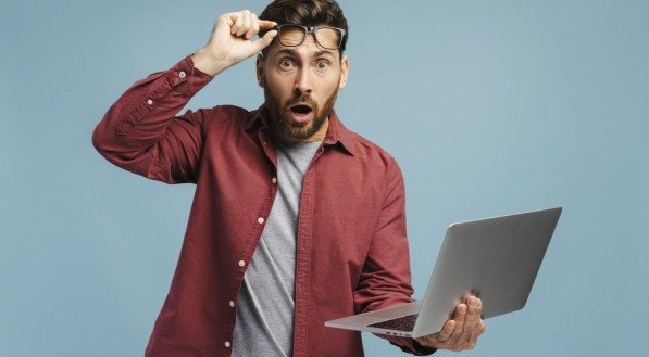 Imagem de um homem com laptop na mão e reagindo com surpresa para novas notícias