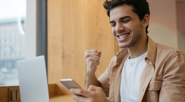 Imagem de um homem segurando o celular e recebendo notícias boas