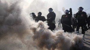 Policiais são vistos através da fumaça na rodovia 101, perto do centro de detenção metropolitano no centro de Los Angeles, domingo, 8 de junho de 2025, após o protesto contra a invasão de imigrantes na noite passada