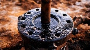 Detalhe de equipamento utilizado na extração de petróleo em campo terrestre; A estrutura está coberta por óleo bruto, evidenciando o momento de vazamento ou início de produção.