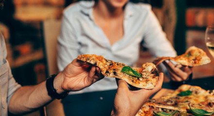 Imagem de pessoas se servindo com pedaços de pizza