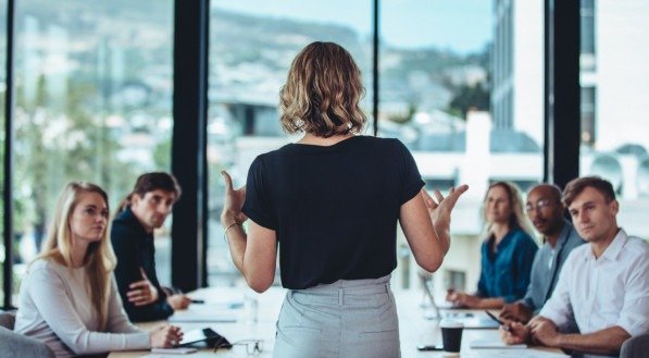 Rear view of a woman explaining new strategies to coworkers during conference meeting in office. Businesspeople meeting in office board room for new project discussion.