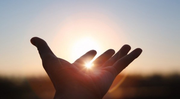 Imagem de mãos estendidas em direção ao sol nascente