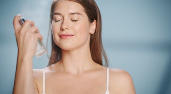 Female Beauty Portrait. Beautiful Caucasian Woman with Brown Hair Using Hydrating Facial Mist Spray Her Natural, Healthy Face Skin. Wellness and Skincare Concept on Soft Isolated Background.