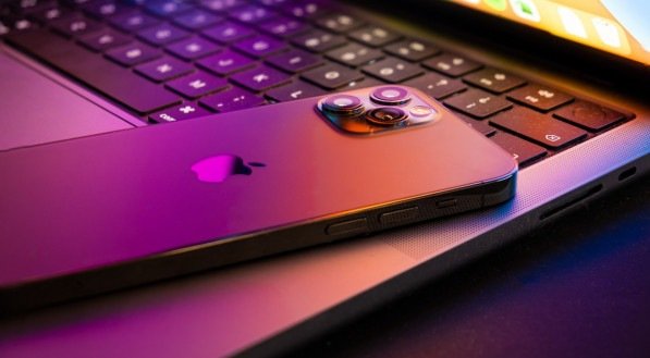 Imagem de um MacBook pro 2021 semiaberto com iPhone 13 iluminado pela tela