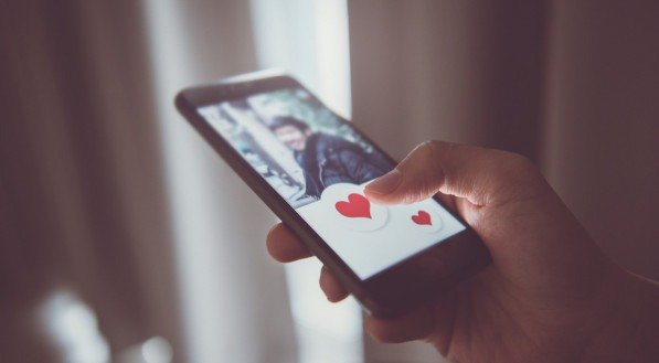 Imagem de uma mão segurando um celular com aplicativo de relacionamento