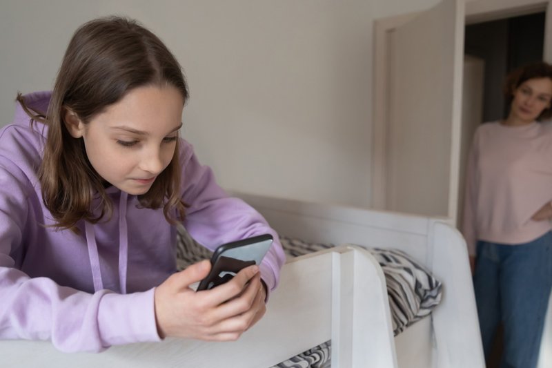 Mãe jovem preocupada controlando adolescente usando smartphone.