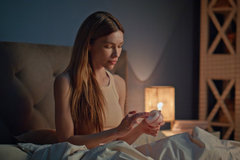 Mulher na cama com produto de beleza na mão