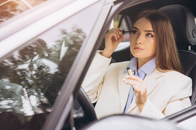 Mulher passando máscara de cílios dentro do carro