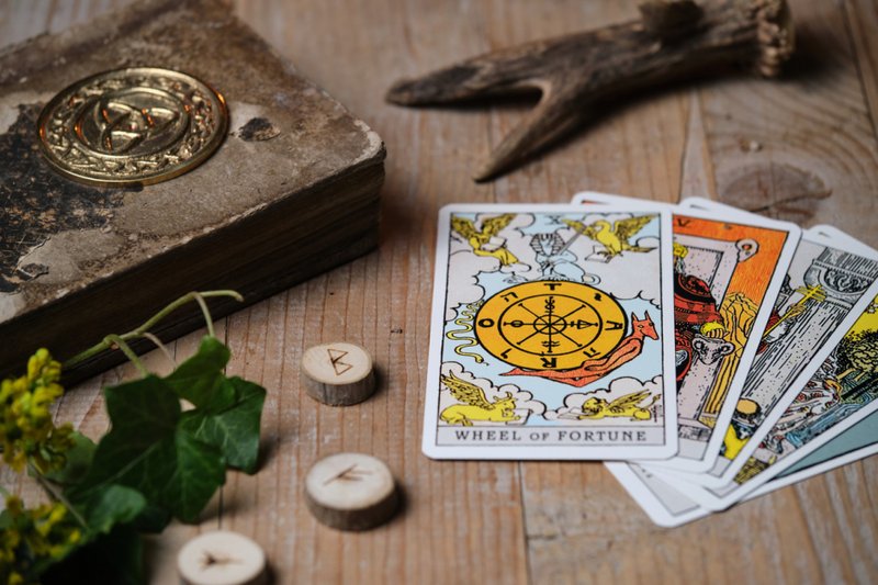 Imagem de cartas de tarô e runas em uma velha mesa de madeira, carta "Roda da Fortuna" colocada no topo