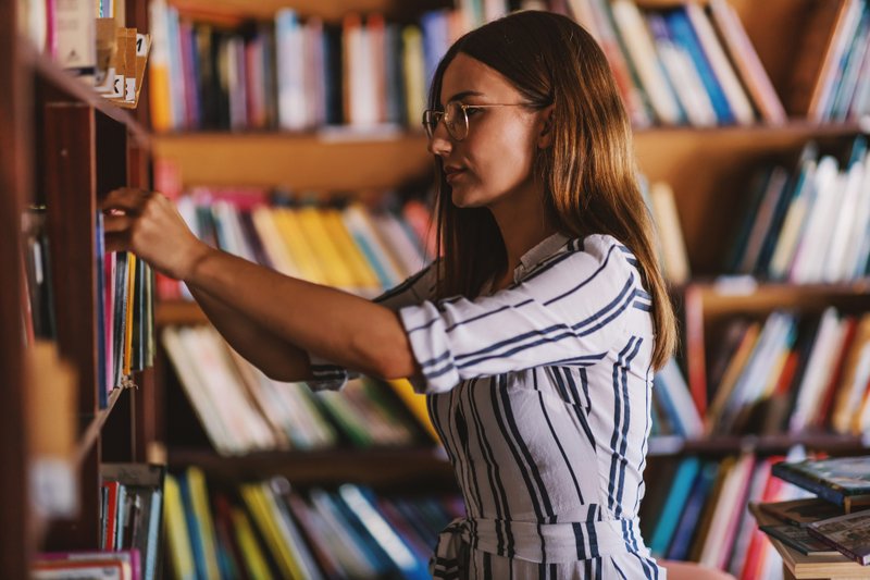 Jovem escolhendo livro da prateleira