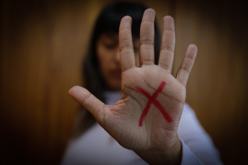 Imagem de uma mulher com a mão em direção à câmera, exibindo um "X" desenhado na palma